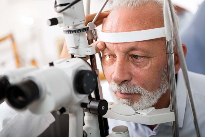 Older man undergoing an eye examination with a slit lamp at an ophthalmologist's office.