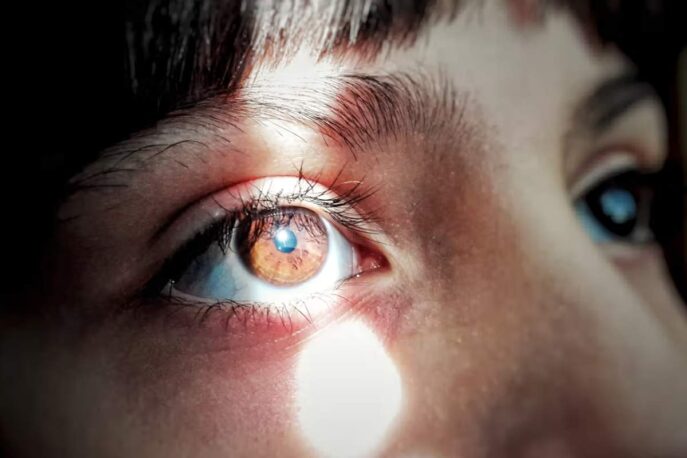 Close-up of a person’s brown eye with a bright beam of light illuminating the iris and reflecting in the pupil.