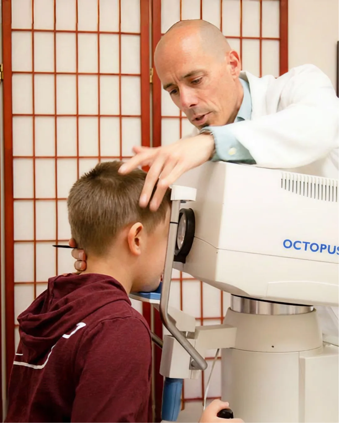 An optometrist performs an eye exam on a young boy in a clinical setting.