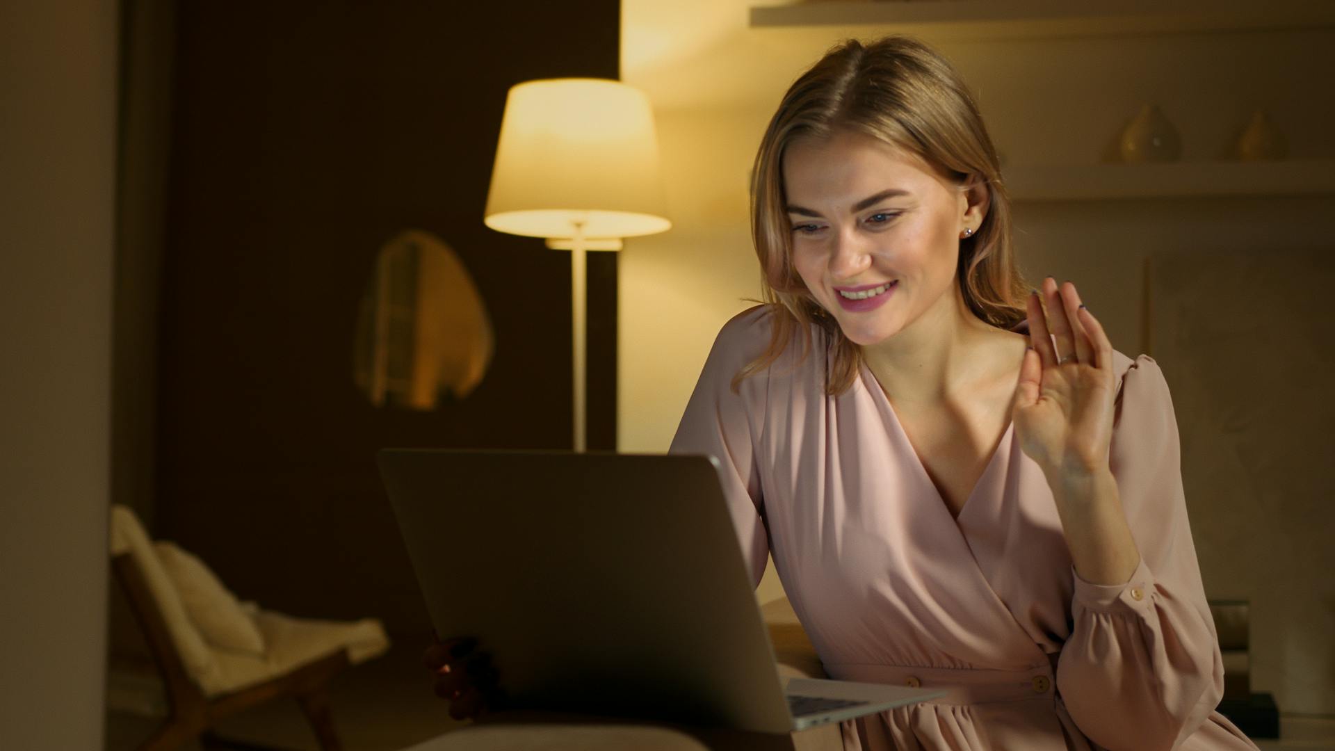 Smiling woman waving at her laptop during a video call at home